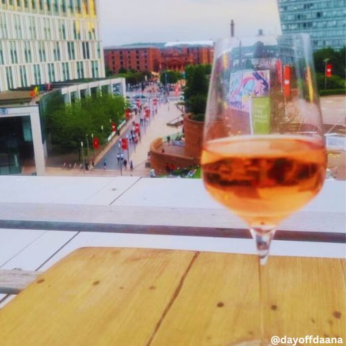 taca de vinho ao canto, cidades ao fundo primeiro a parte renovada da cidade, onde acontecem eventos e fica um shopping a ceu aberto e ao fundo area do centro historico de liverpool