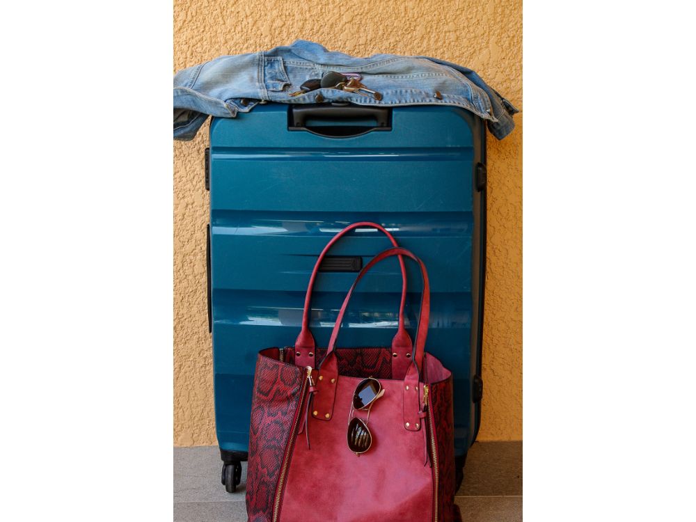 mala azul, jaqueta, chaves e bolsa rosa ao lado simbolizando bagagem extra
