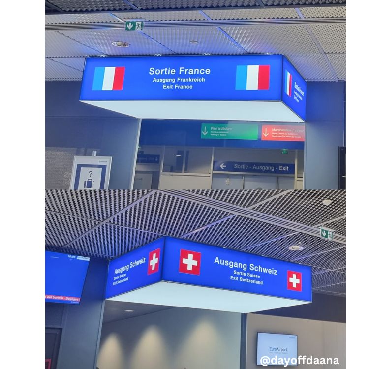 laca no Aeroporto de Basel com duas saídas: na parte superior, saída para a França, com inscrições em francês, alemão e inglês; na parte inferior, saída para a Suíça, com inscrições em alemão, francês e inglês.