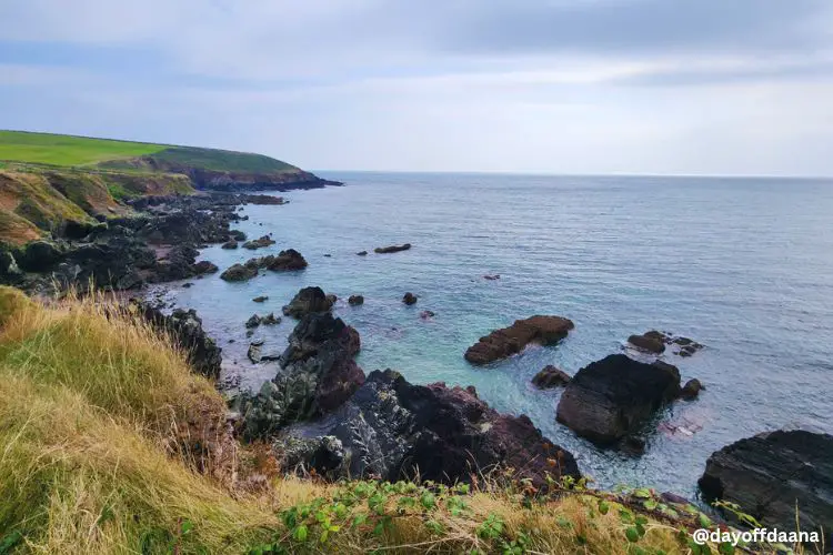 Alt =Ballycotton Cliff Walk -Mostrando vista da caminhada com mar, pedras e verde no alto com longo caminho