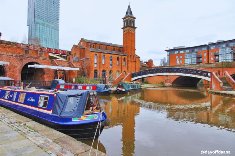Bairro de Manchester com rio à frente, construções industriais históricas nas margens e, ao fundo, edifícios modernos criando um contraste especial.