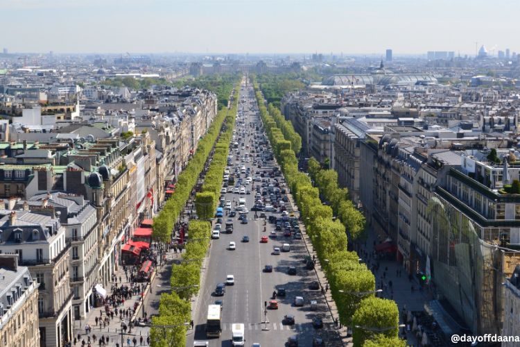 Alt: A Champs-Élysées, uma avenida movimentada, cheia de carros e comércios, mas ainda assim arborizada. Um local que não pode faltar na sua lista do que fazer em Paris.