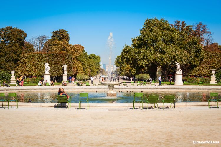 Alt: Foto mostra uma fonte no centro, algumas esculturas e cadeiras para sentar e relaxar. Ao fundo, uma paisagem verde.