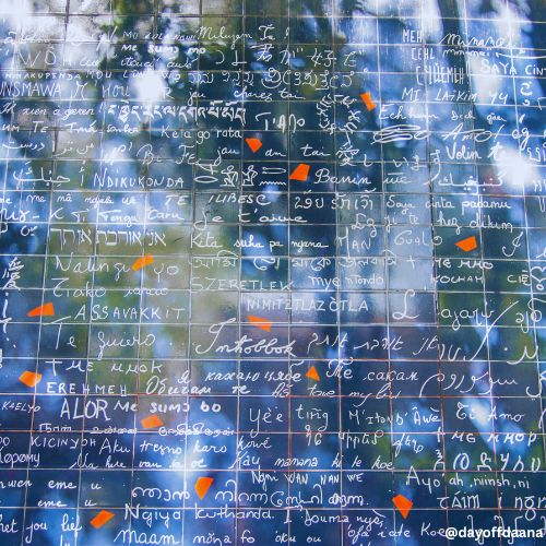 Alt: Parte do muro de azulejos azuis com escritos em branco e detalhes vermelhos, uma visita romântica e inspiradora para fazer em Paris