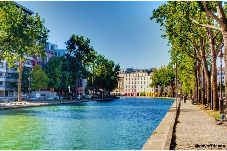 Alt: Canal Saint-Martin – uma opção para passear, se divertir e apreciar a cultura local. Foto mostra o rio, caminho arborizado e casas ao redor.