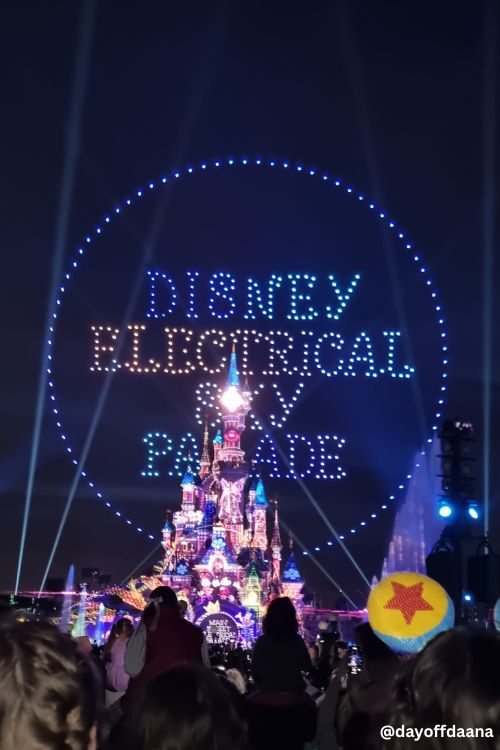 Foto mostra castelo iluminado com drones que iluminam o ceu e escrito Disney Electrical Sky Parade