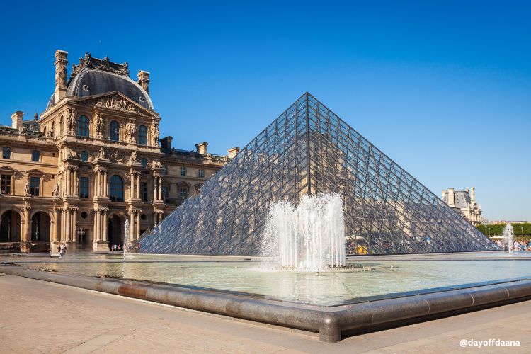 Alt: Vista da pirâmide de vidro do Louvre com o museu ao fundo – um dos símbolos clássicos de Paris.