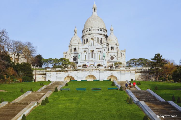 Alt: Basílica de Sacré-Cœur, com escadarias e gramados ao redor, um clássico que não pode faltar na sua lista do que fazer em Paris. A basílica em estilo românico, em pedra branca, é ainda mais charmosa no outono.