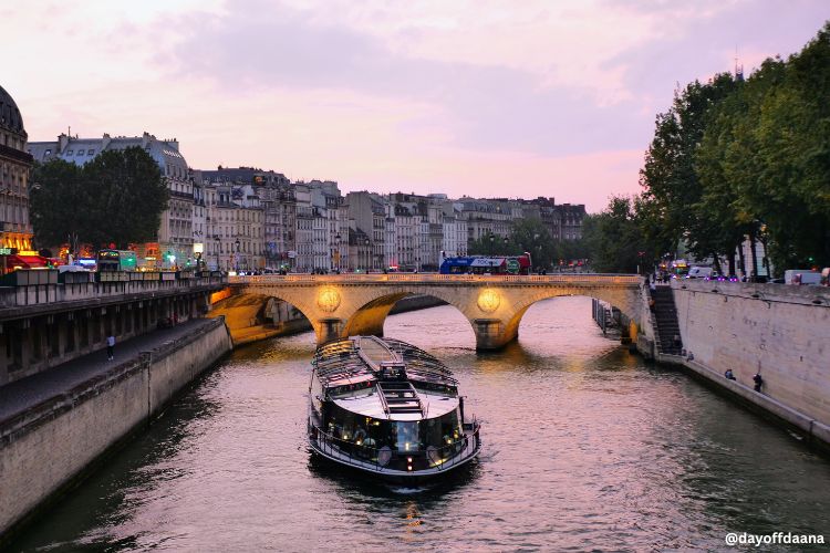 Alt: Entardecer em Paris com barco passando pelos principais pontos turísticos da cidade de Paris.