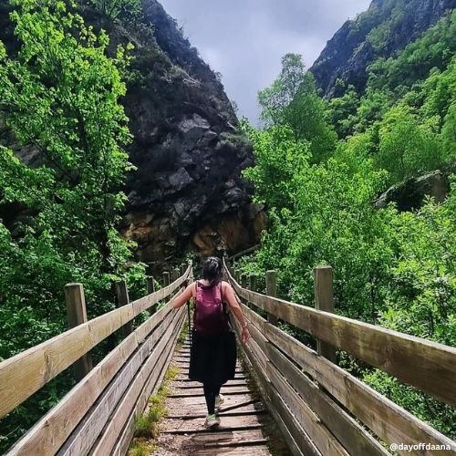 Estou no meio com mochila, sozinha em meio as montanha e uma ponte. Viajar sozinha e importante e te conecta
