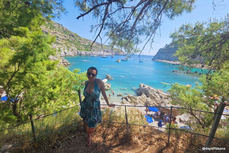 praia anthony quinn- dayoff praia Anthony Quinn Bay vista ao lado, agua bem clara com pedras em volta, eu estou na frente com vestido azul.