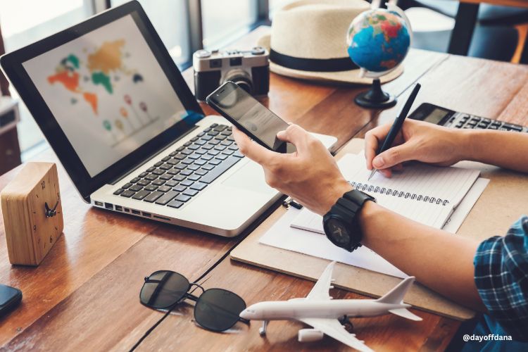 pessoa planejando viagem com celular, computador na mao e notebook